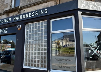 Exterior of Perfection Hairdressing in Kirkcaldy, Scotland, GB, highlighting salon signage and glass windows.