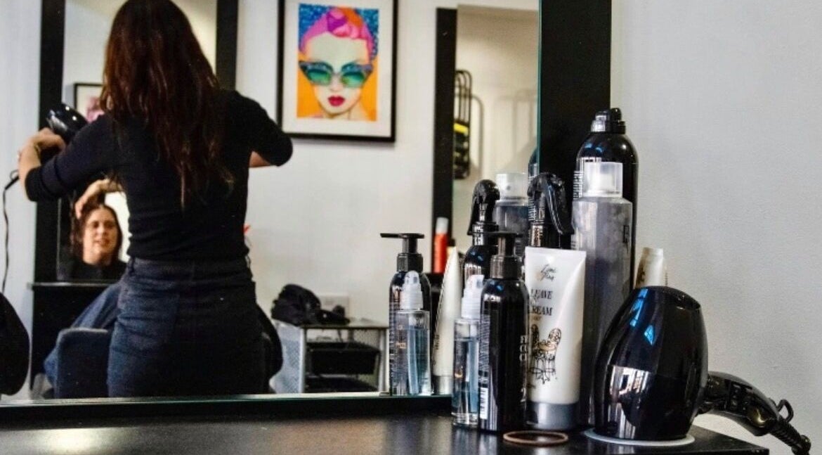 Stylist working on client's hair at Zest Studio, Colchester, England, GB, reflected in a mirror with products in view.