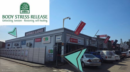 Exterior of Hartenbos Body Stress Release in Mossel Bay, Western Cape, ZA, showcasing nearby businesses.