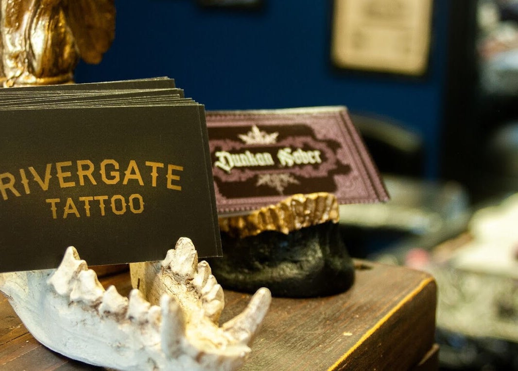 Business cards at Rivergate Tattoo, Luton, England, GB, showcasing a stylish design on a rustic stand.