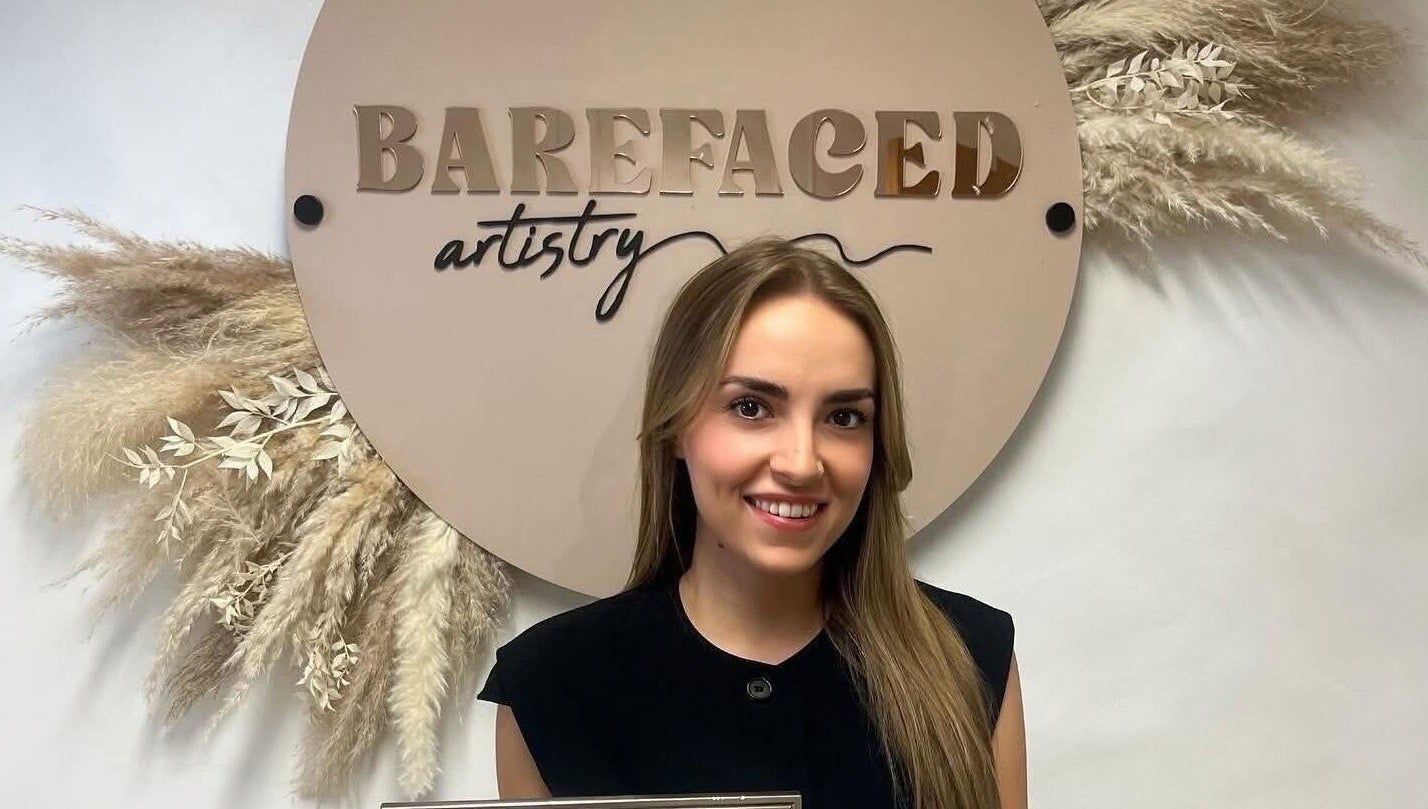 Smiling artist at Barefaced Artistry, Hilton, England. Elegant sign with floral accent.