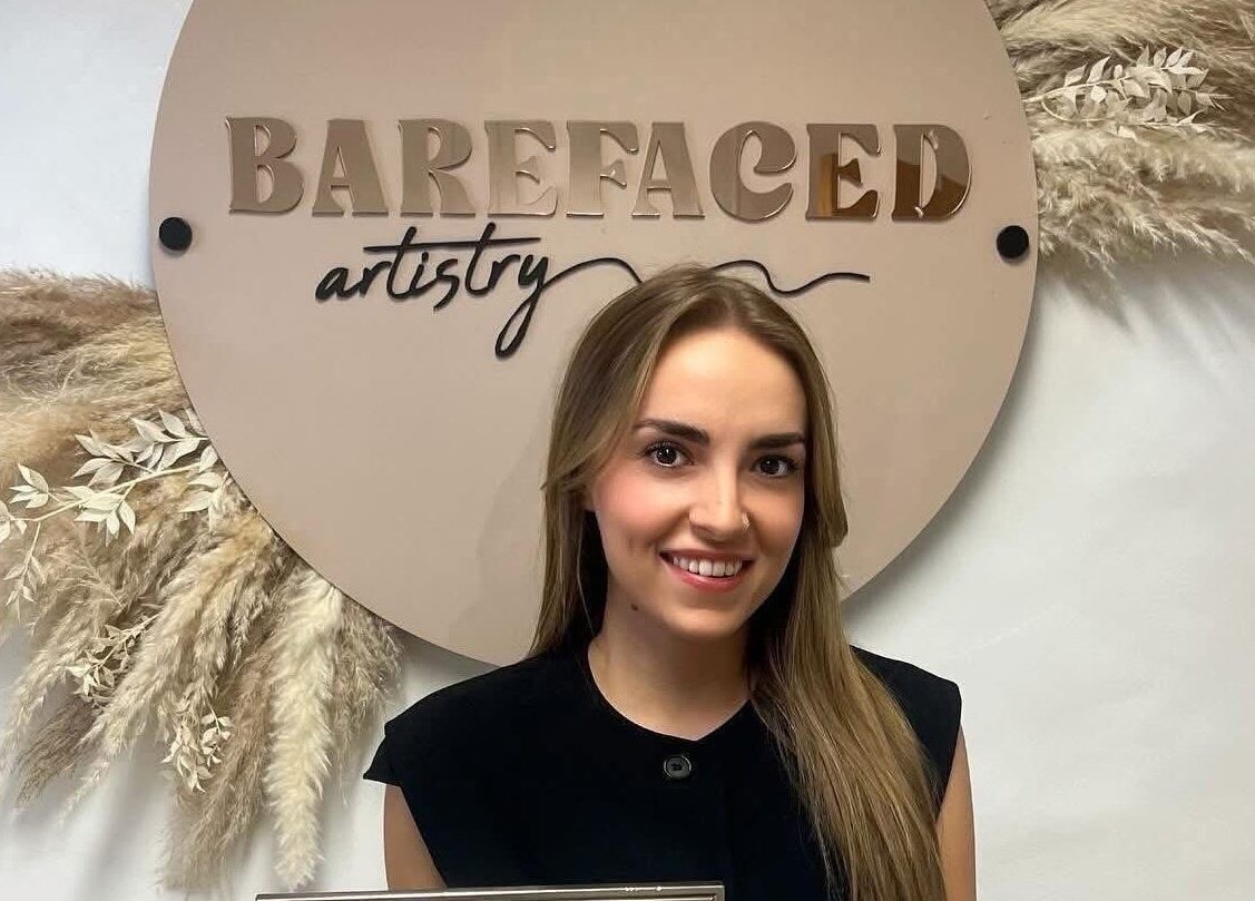 Smiling artist at Barefaced Artistry, Hilton, England. Elegant sign with floral accent.
