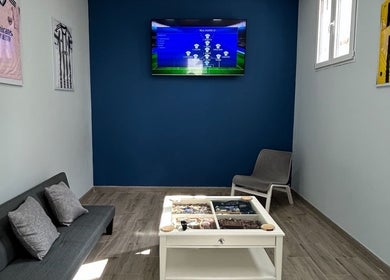 Acogedora sala de espera en BladesColor Reus, Reus, Catalunya, ES, con sofá, televisor y decoración futbolística.