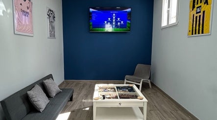 Acogedora sala de espera en BladesColor Reus, Reus, Catalunya, ES, con sofá, televisor y decoración futbolística.