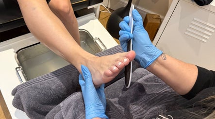 Foot care at Polished Nails, Portsmouth, England, GB. Blue-gloved hands perform a pedicure on a foot.