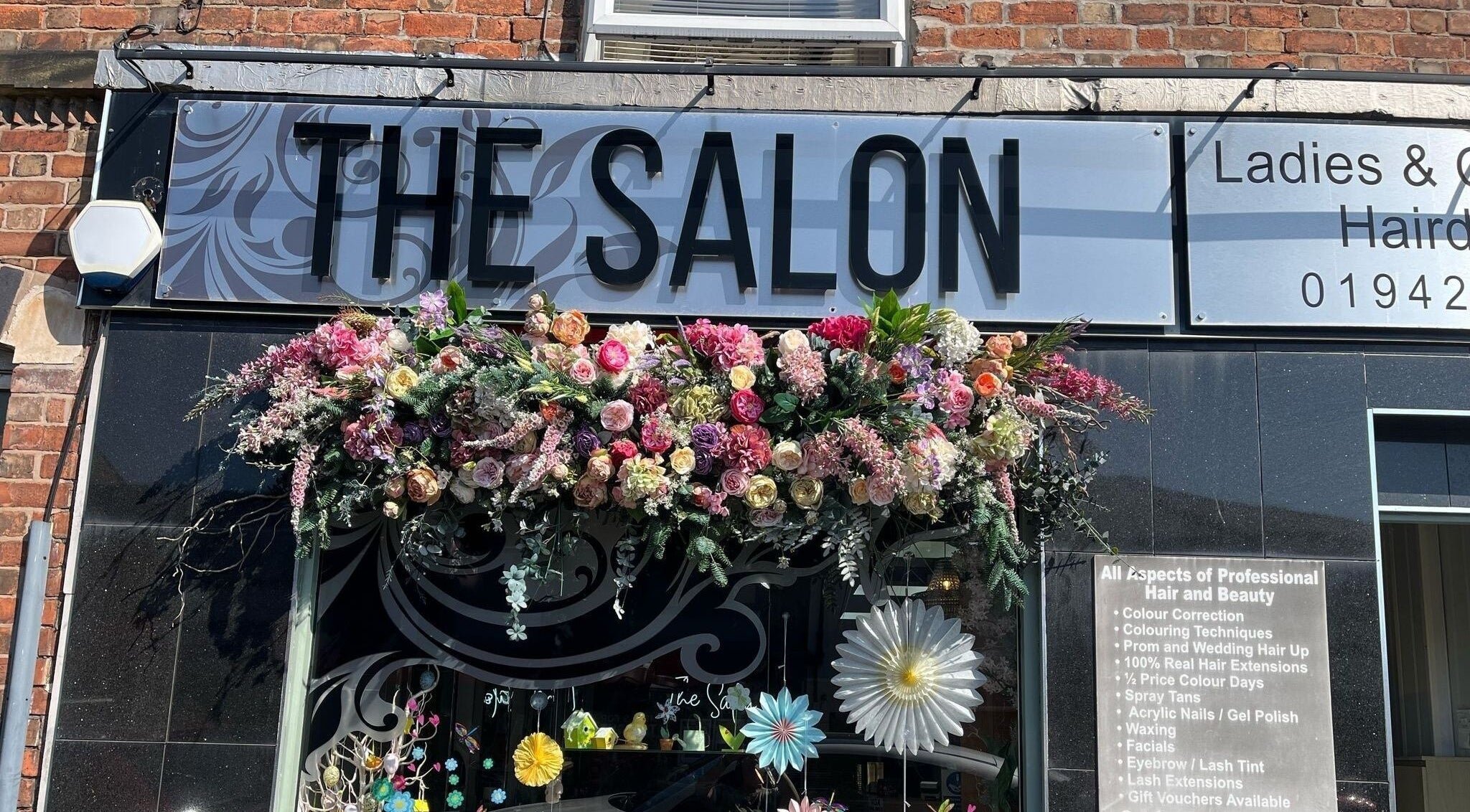 The Salon in Wigan, GB with a vibrant floral display adorning the entrance sign.