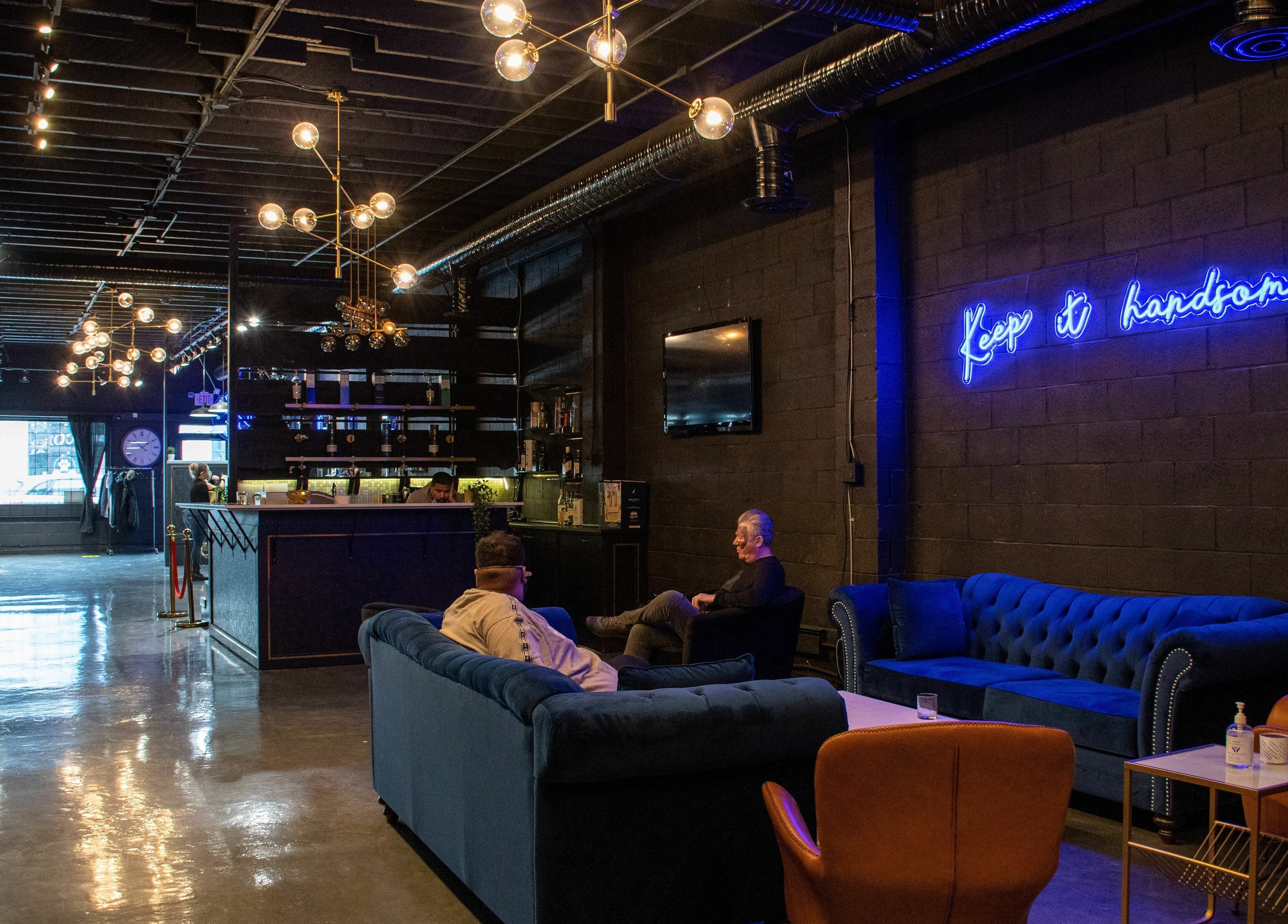 Chic interior of Scotch and Fades in Vancouver, BC, with modern couches and neon sign.
