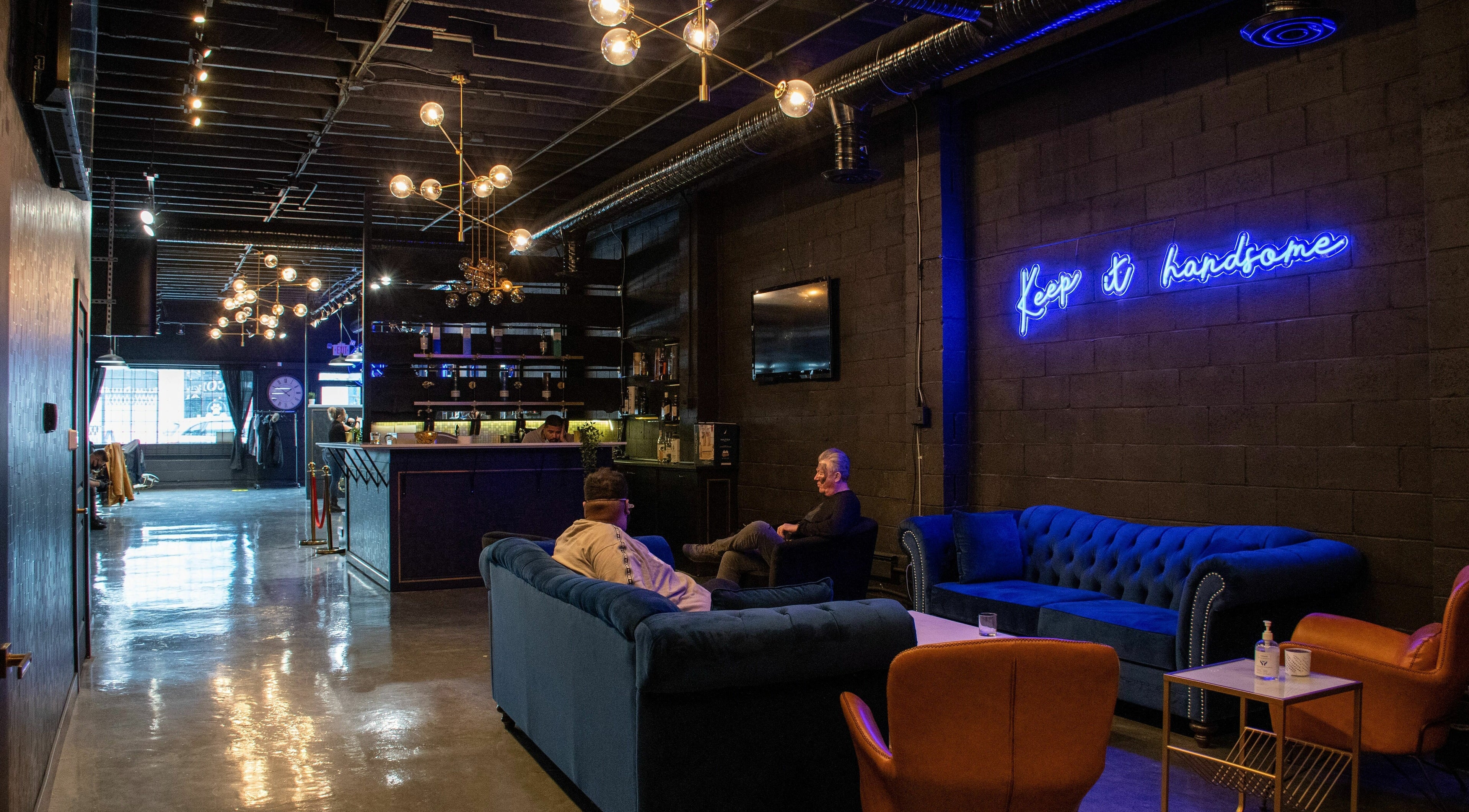 Chic interior of Scotch and Fades in Vancouver, BC, with modern couches and neon sign.
