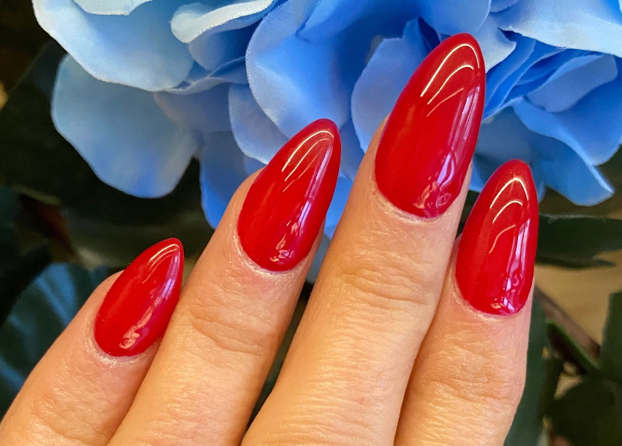 Vibrant red manicured nails with blue flower backdrop at Nails By Jo, Fremington, England, GB.