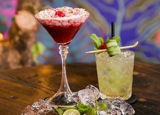 Colorful cocktails at Blow Bar Bali, Bali, ID on a wooden table with a vibrant background.