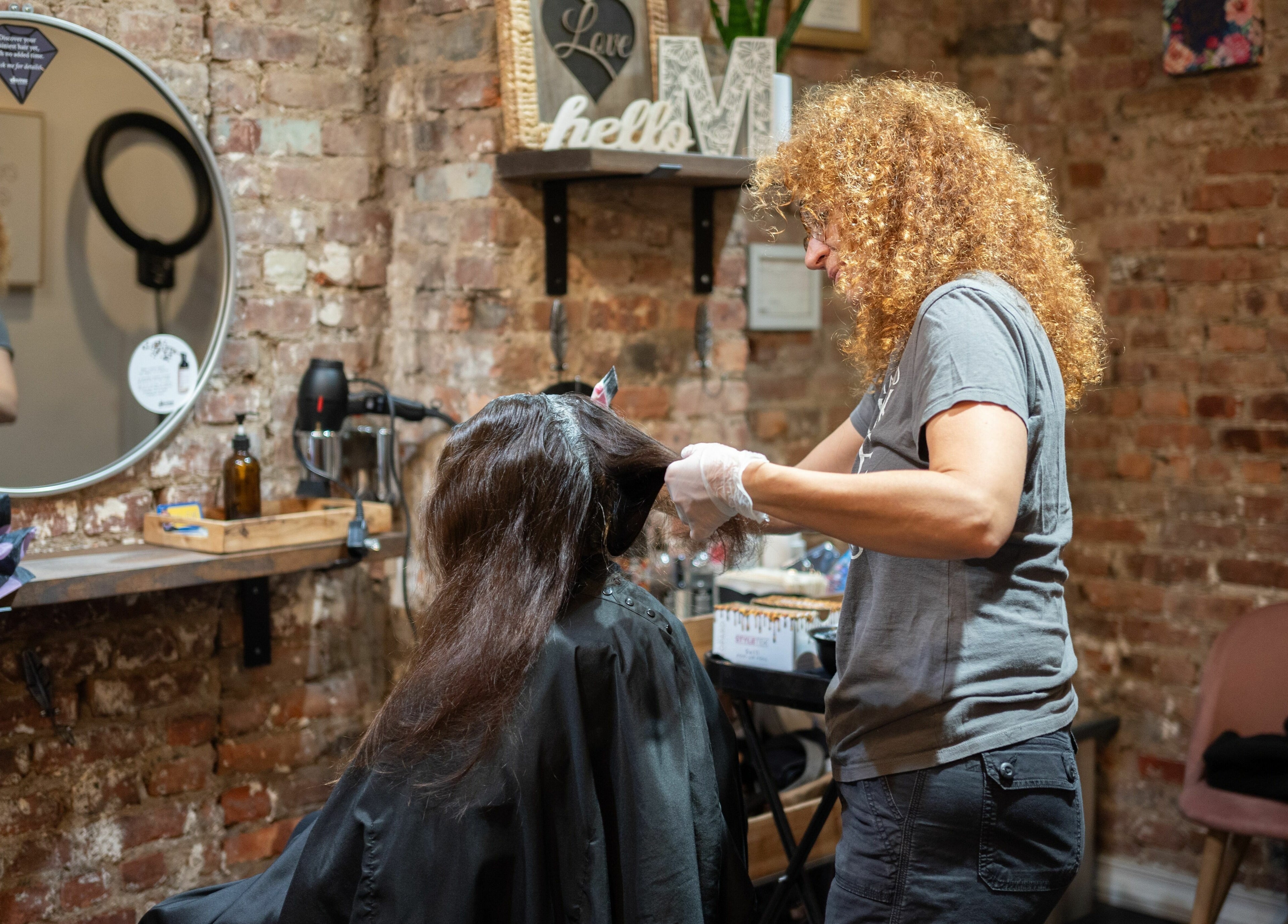 Stylist at David Ryan Salon in New York, New York, US, expertly colors client's hair against rustic brick walls.