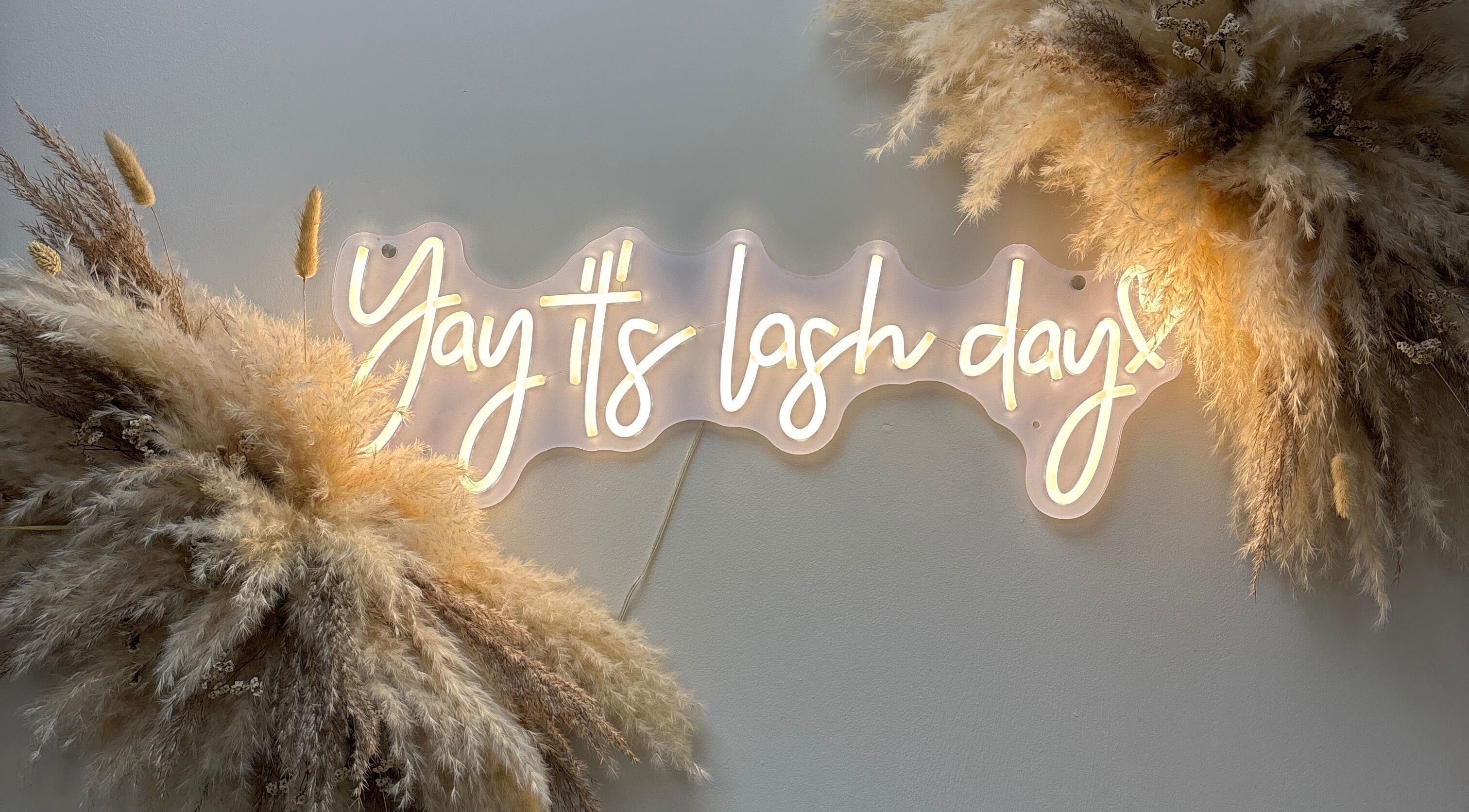 Neon sign saying 'Yay it's lash day' at Carly Mendes At Art House, Burnley, England, GB, with soft pampas decor.