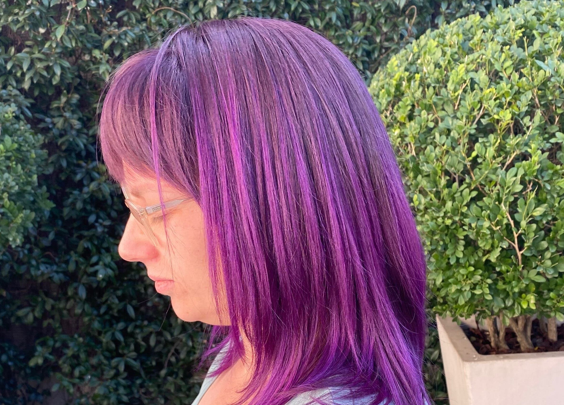 Vibrant purple hair styled at Ilze at Makeup Madonna, Wellington, Western Cape, ZA. Lush greenery in background.