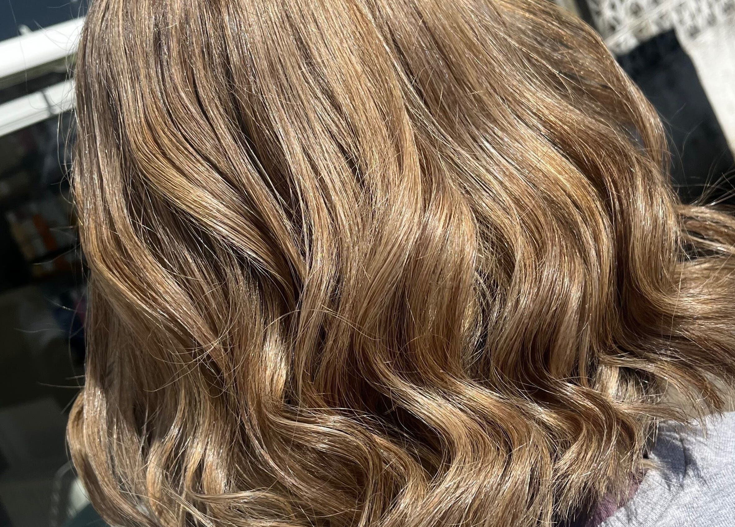 Golden wavy hairstyle at Polgooth Village Salon, Polgooth, England, GB. Shiny texture highlights expert hairstyling.