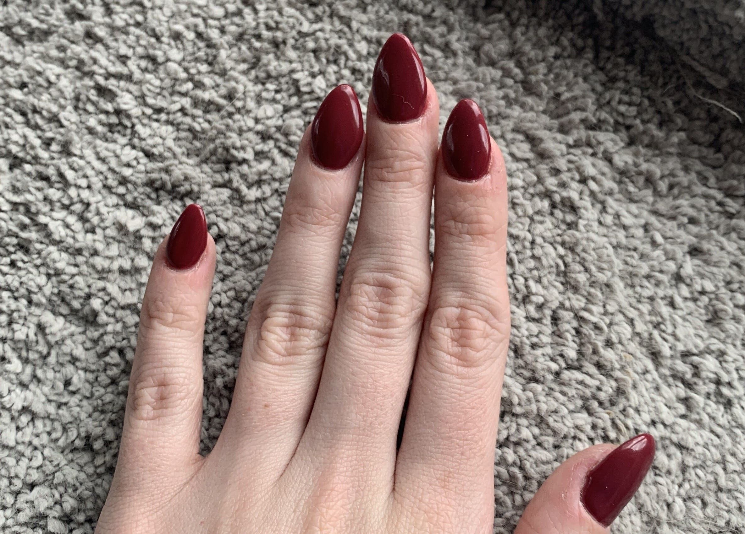 Stylish crimson nails from Elegant Nails and Spa, London, Ontario, CA. Manicured hand on textured carpet.