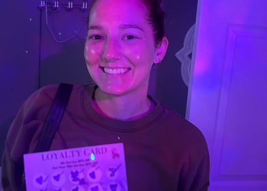 Happy visitor at Hannah’s Lilac Room, Mccordsville, Indiana, holding a loyalty card under soft purple lighting.