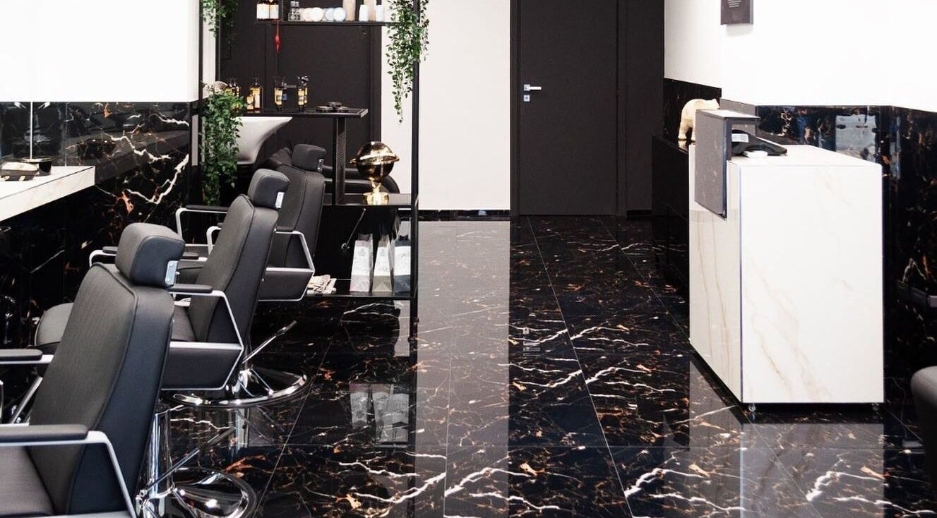 Interno elegante del BELMORE HAIR STUDIO, Bari, Puglia, IT, con sedie nere e dettagli di marmo.