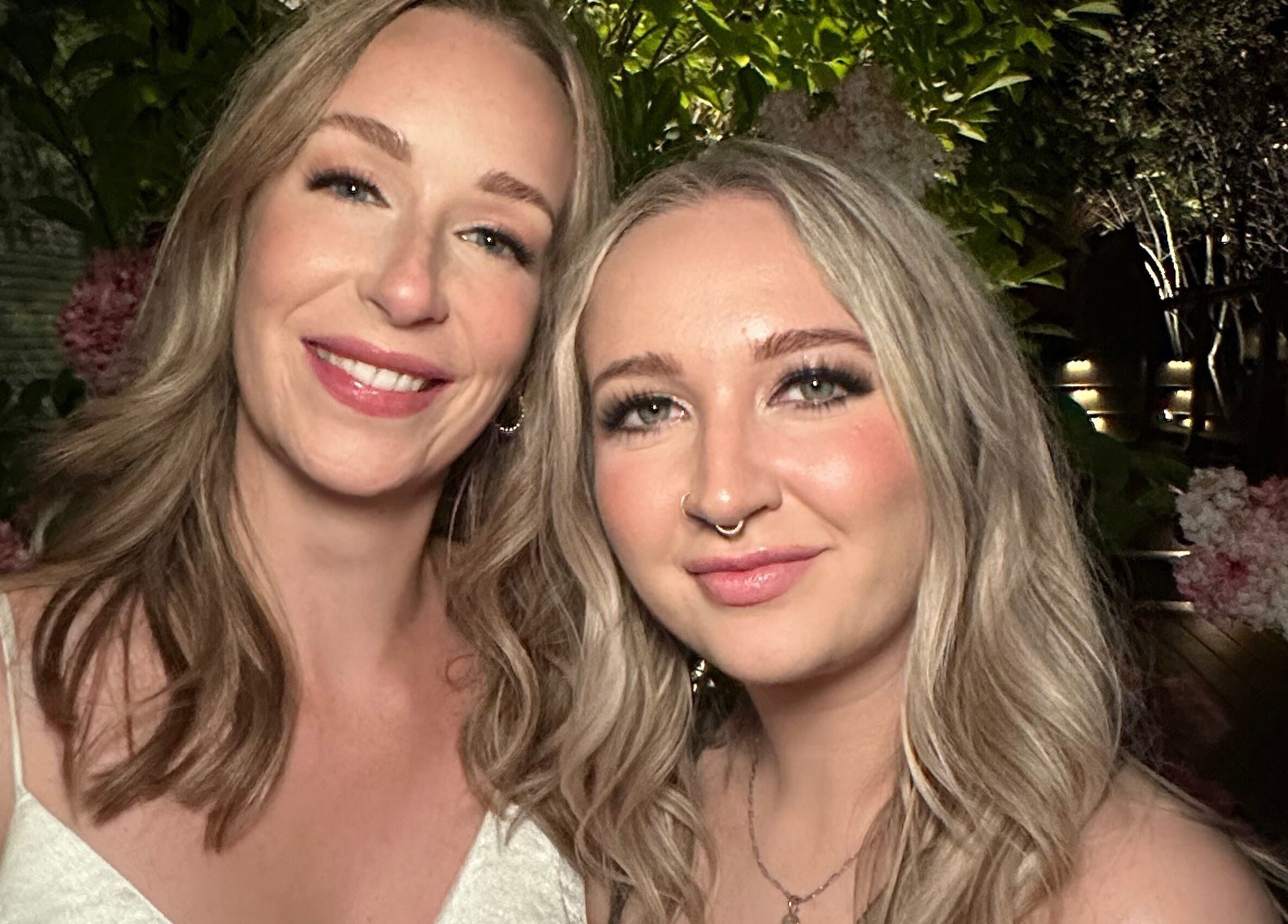 Two women smiling amid lush greenery at Glam By Shan, Newmarket, Ontario, CA.