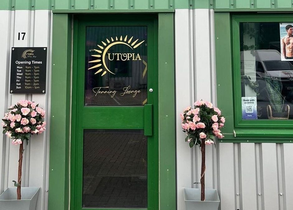 Entrance of Utopia Wymondham in Wymondham, England with green door, floral decor, and opening hours.