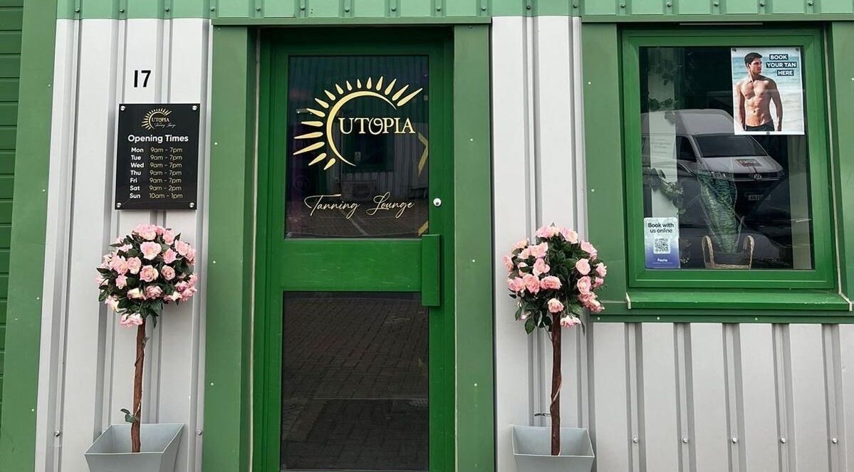 Entrance of Utopia Wymondham in Wymondham, England with green door, floral decor, and opening hours.