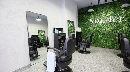 Sleek black barber chairs in front of a green wall at Sonder Mens | Bondi Junction, New South Wales, AU.