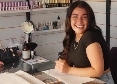 Nail technician smiling at LP Extensions, Fordingbridge, England, GB, showcasing vibrant nail polishes.