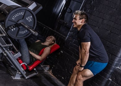 Personal trainer assisting client during leg press at Kiwi Personal Training, Manchester, England, GB.