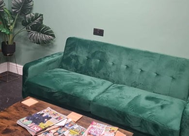 Cozy green sofa at The Green Lounge, Haughley, England, GB, with magazines and potted plants enhancing tranquility.