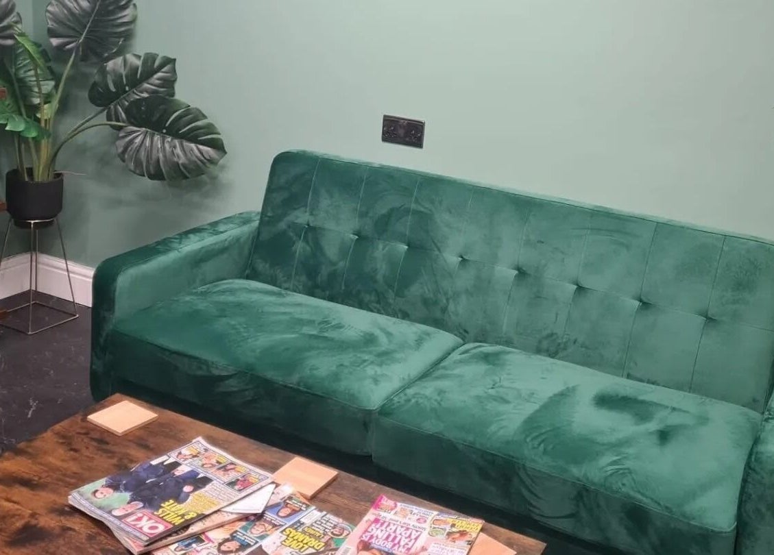 Cozy green sofa at The Green Lounge, Haughley, England, GB, with magazines and potted plants enhancing tranquility.