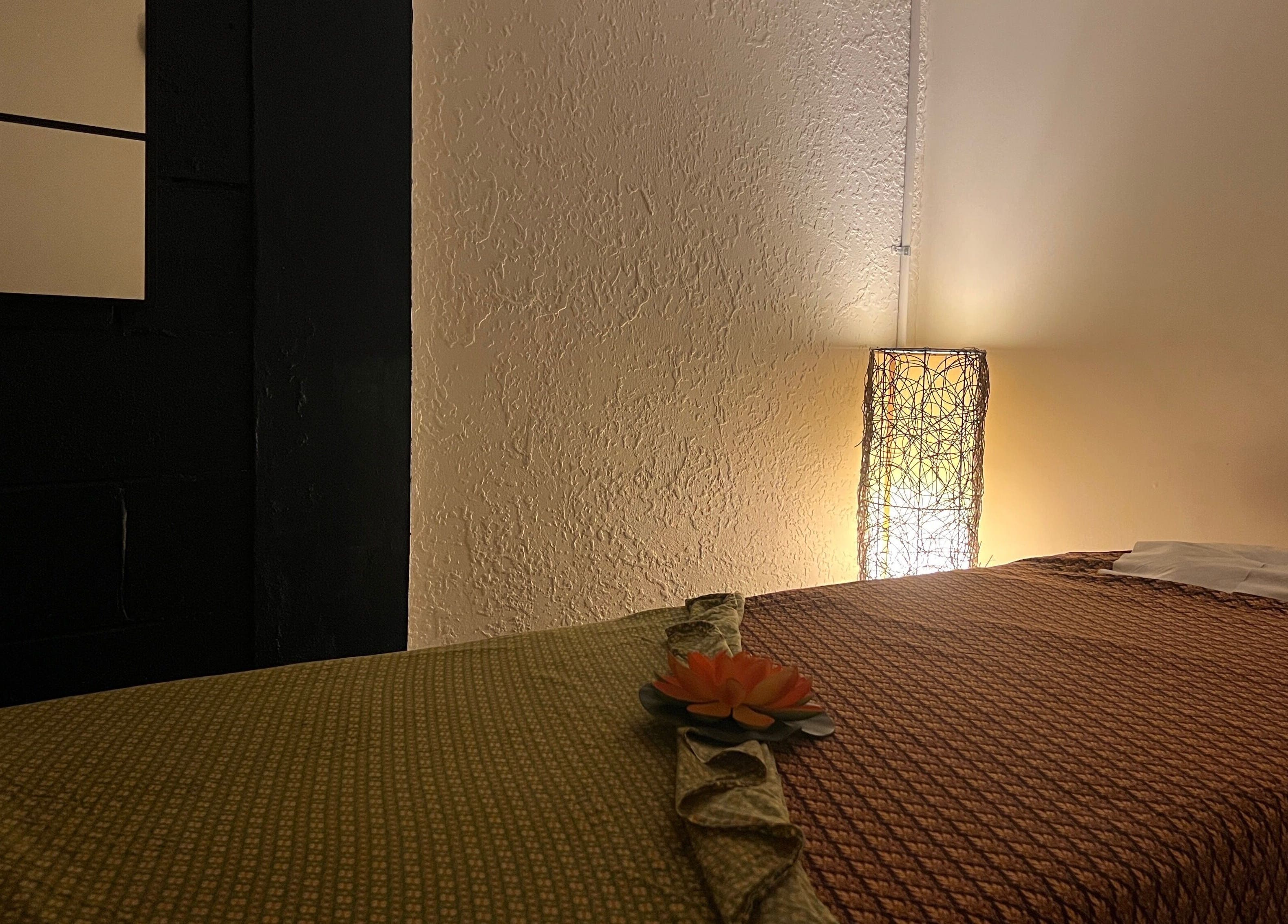 Tranquil massage room at Fern Spa & Massage, Auckland, NZ with ambient lighting and flower on bed.