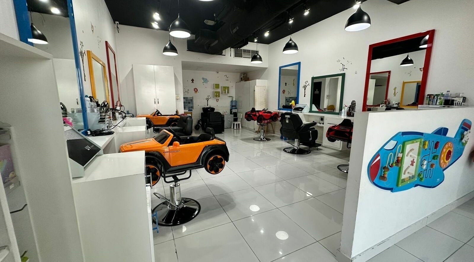 Interior of Cute Kids Saloon in Dubai, AE featuring playful car-themed chairs and colorful decor.
