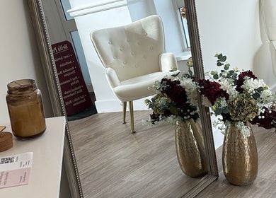 Elegant interior with a white chair at By Leah, Whitley Bay, England, GB, showcasing floral decor and a large mirror.