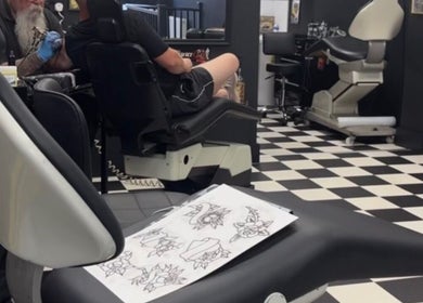 Tattoo artist working at G’lamore Ink & Beauty, Birmingham, England, GB, with designs on display.