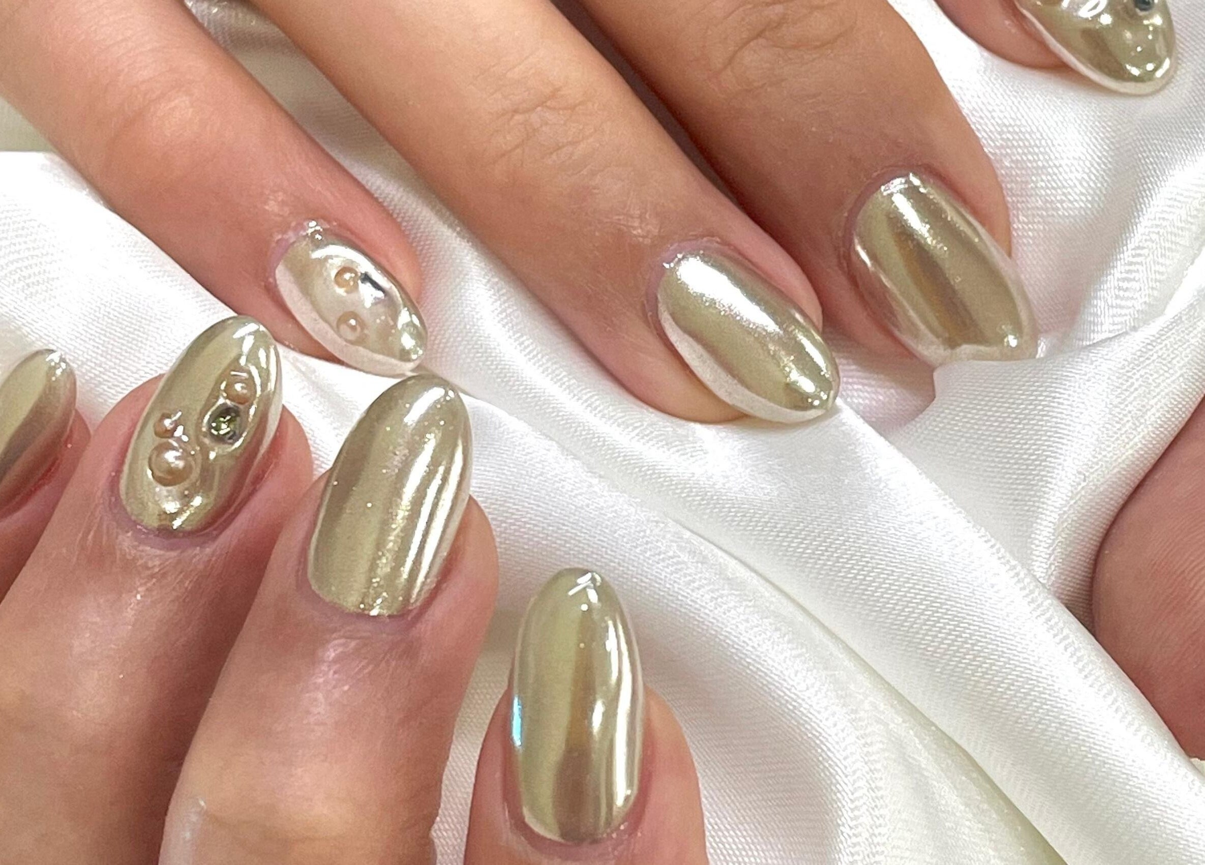 Elegant pearl-accented gold nails at Allurix Nail Salon, Singapore, Singapore, SG, on silky white fabric.