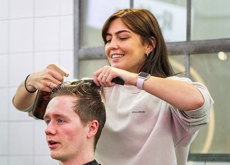 Hair stylist giving a haircut at Rythm Studio, Bristol, England, GB. Smiling professional creating stylish look.