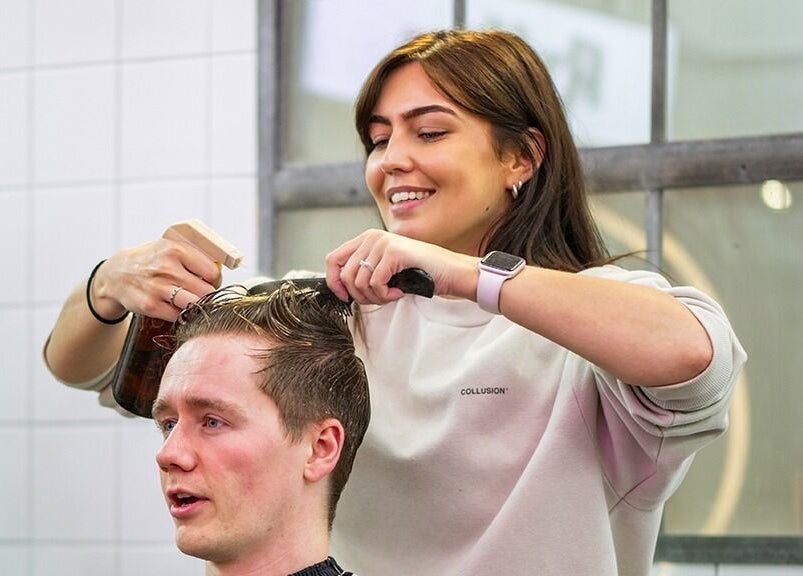 Hair stylist giving a haircut at Rythm Studio, Bristol, England, GB. Smiling professional creating stylish look.