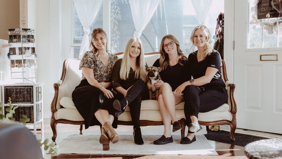 The Beauty Loft team at Marmora, Ontario CA, smiling on a vintage sofa with a dog.
