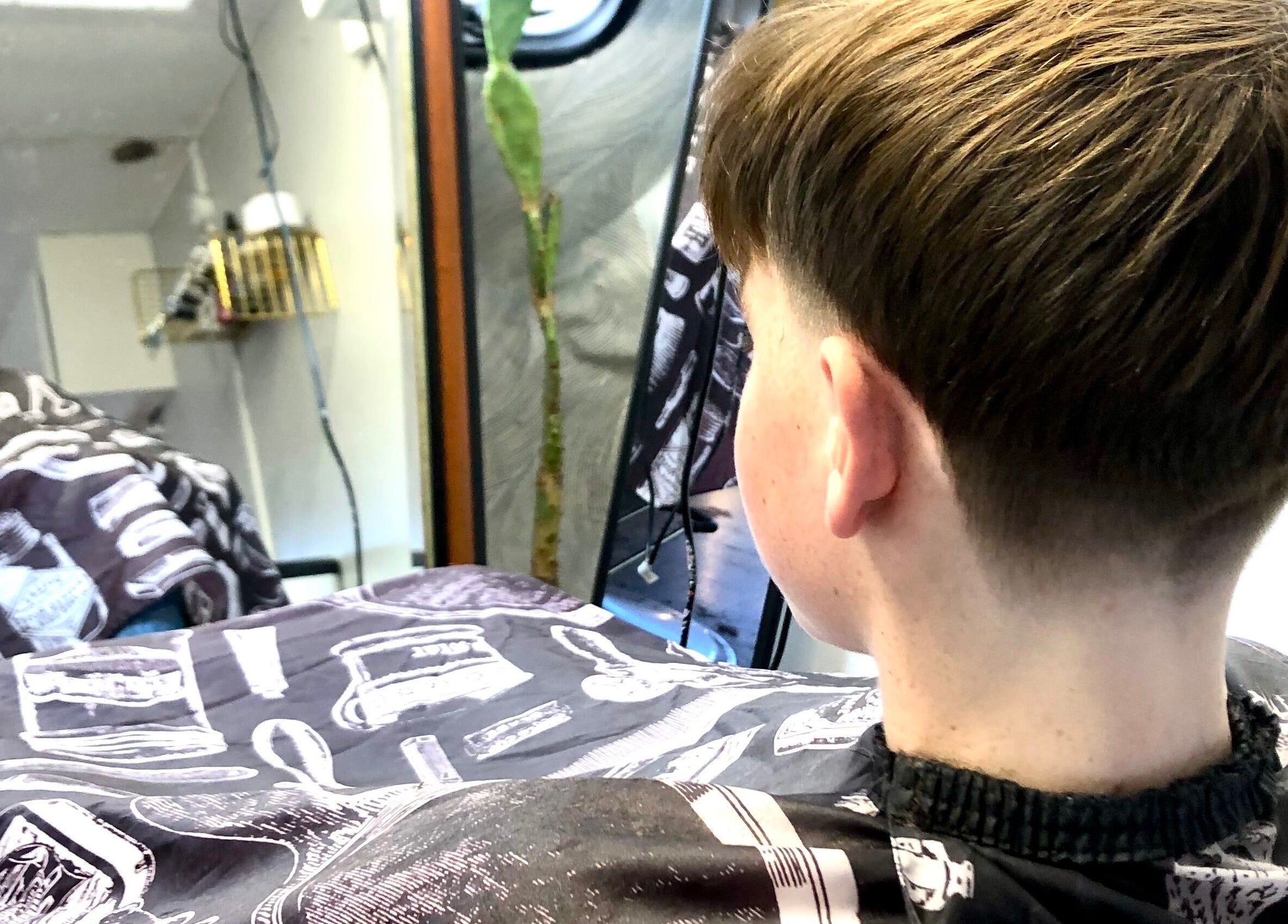 A young boy admires his haircut in the mirror at The Barber Hut, Portrush, Northern Ireland, GB.