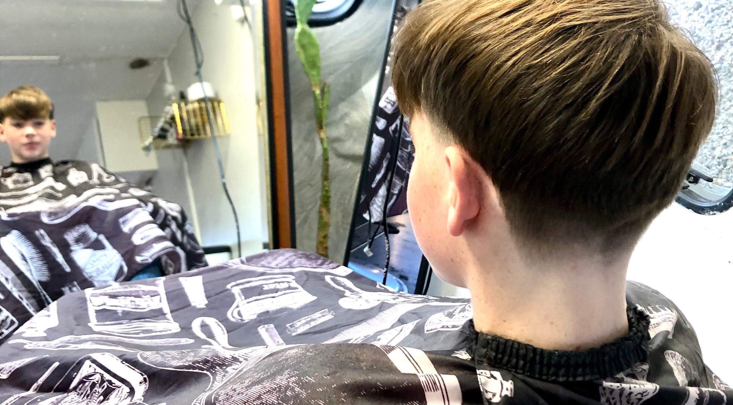 A young boy admires his haircut in the mirror at The Barber Hut, Portrush, Northern Ireland, GB.