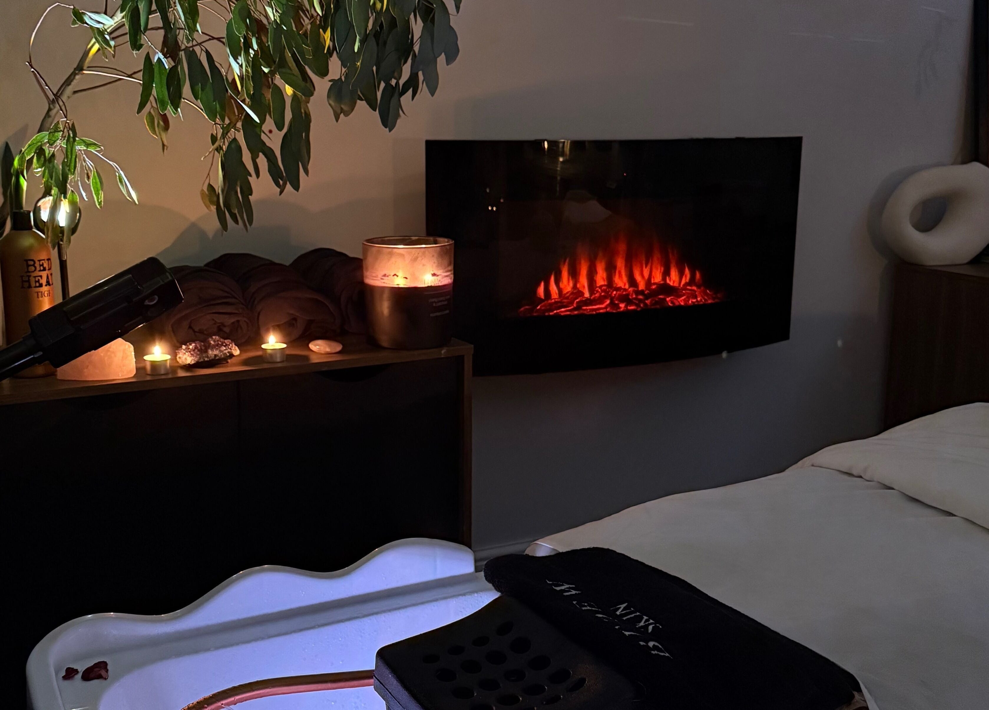 Relaxing spa corner at The Signature Edit - Bedew Skin, Corby, England, GB, featuring candles and a warm fireplace.