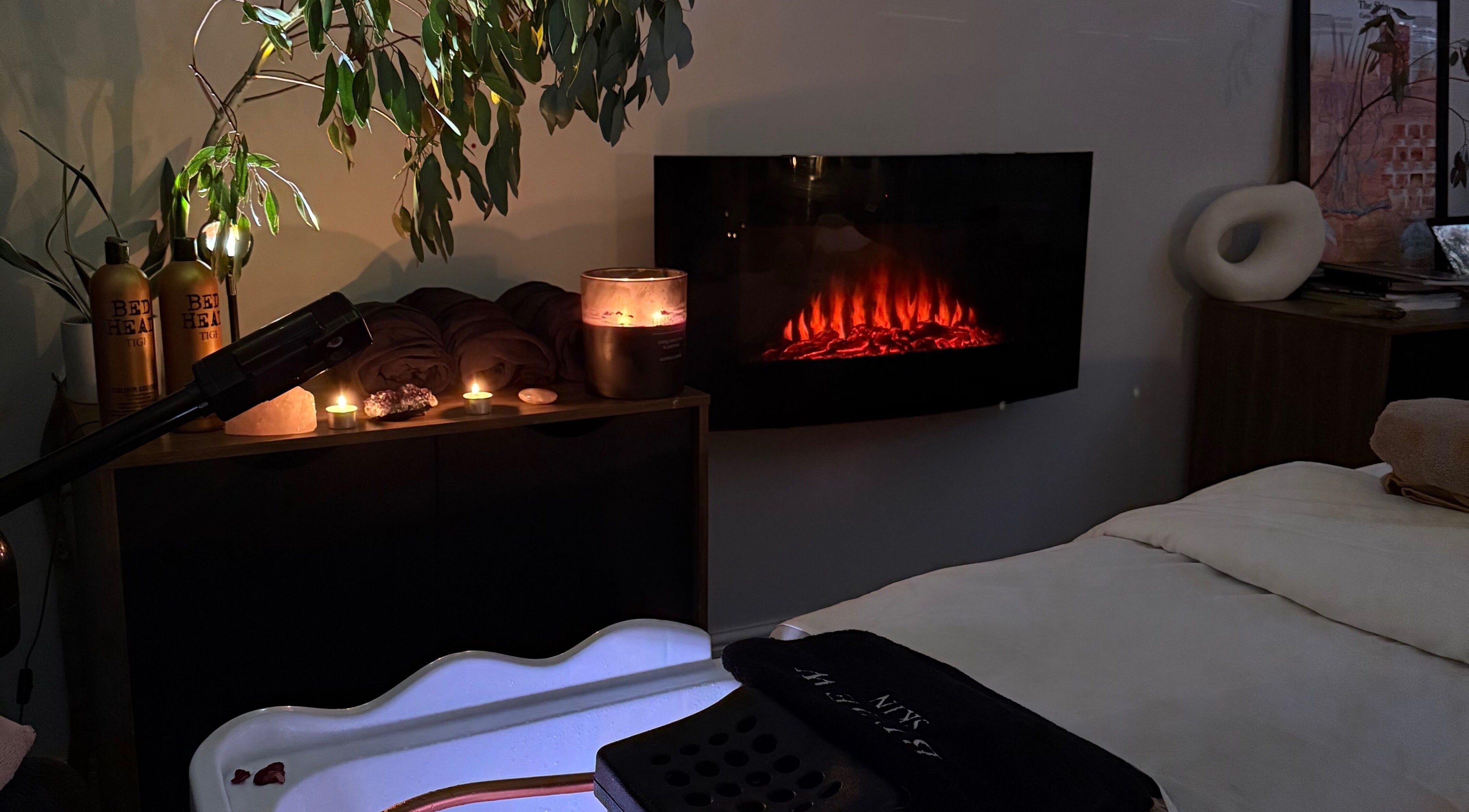 Relaxing spa corner at The Signature Edit - Bedew Skin, Corby, England, GB, featuring candles and a warm fireplace.