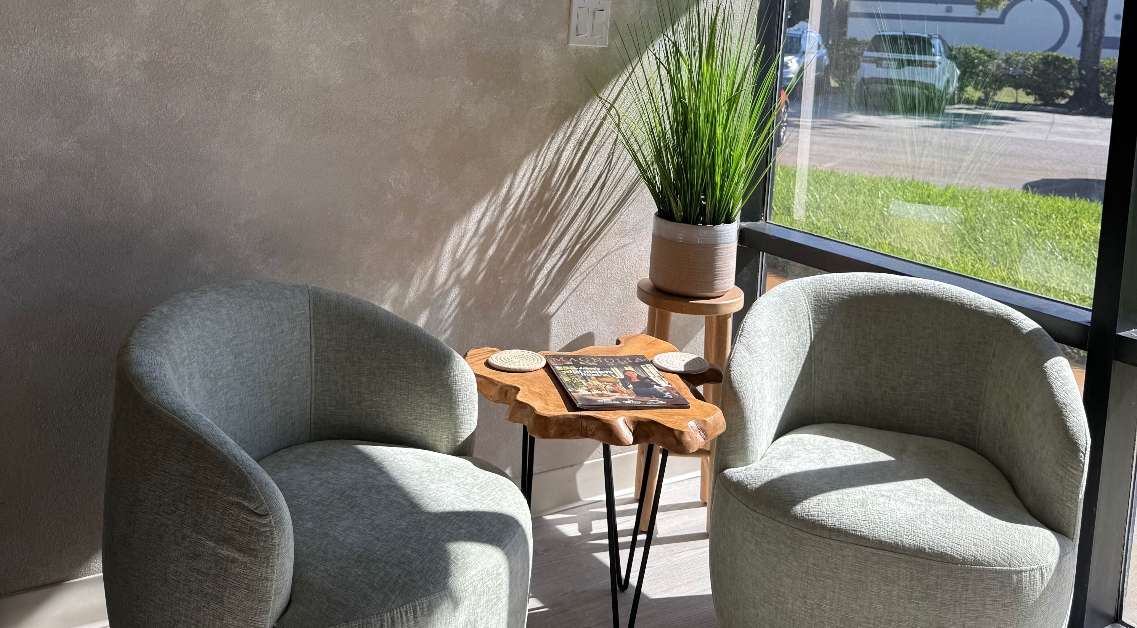Two green chairs with a wooden table at Curated Color & Extensions, Tampa, Florida, US.