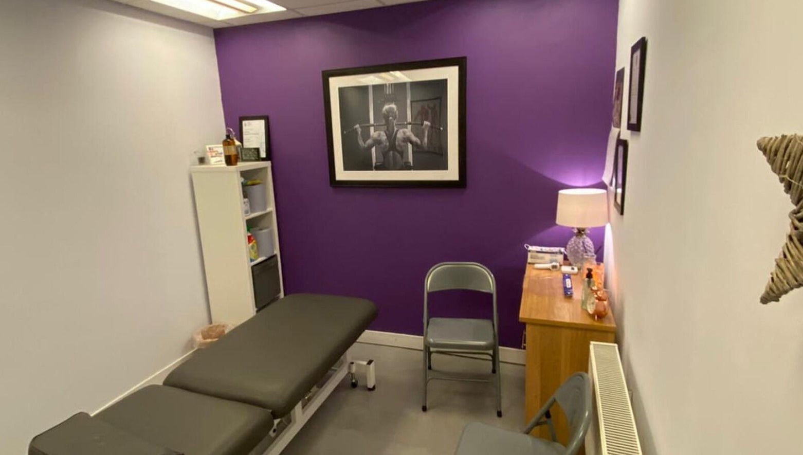 Cozy therapy room at Molly Sports Massage, Locker 27, Addlestone, England, with purple accent wall and massage table.