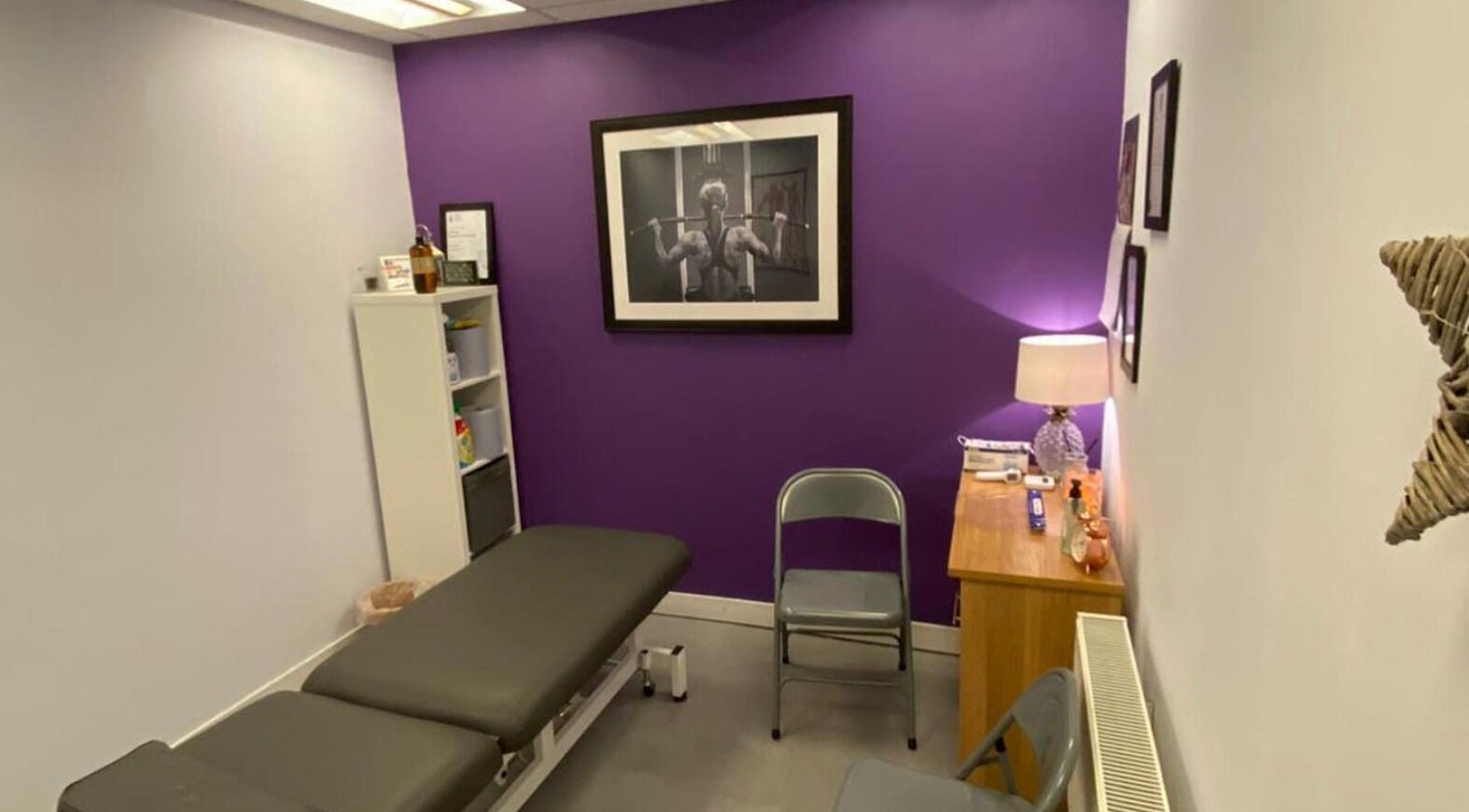 Cozy therapy room at Molly Sports Massage, Locker 27, Addlestone, England, with purple accent wall and massage table.