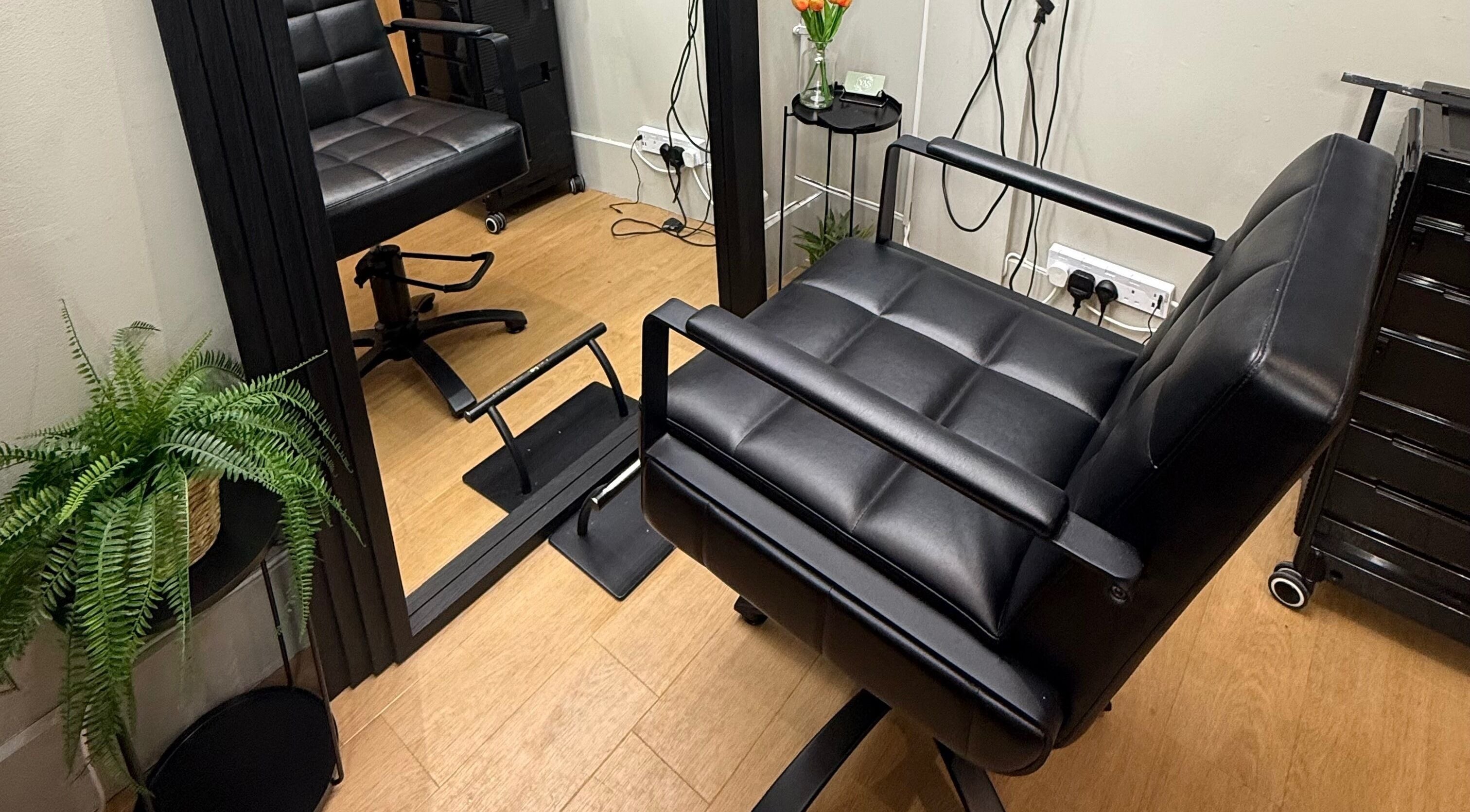 Modern salon chair at Yas Did My Hair, Bedford, England, GB, surrounded by mirrors and greenery.