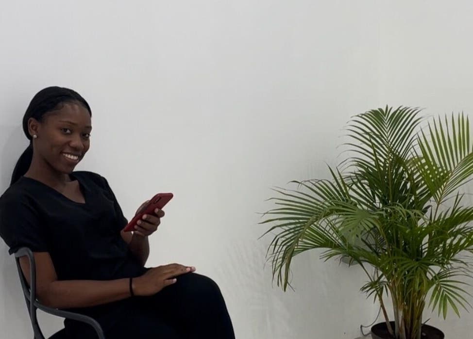 Smiling person sitting by plant at Jahzeni Beauty Lounge, Runaway Bay, St. Ann Parish, JM.