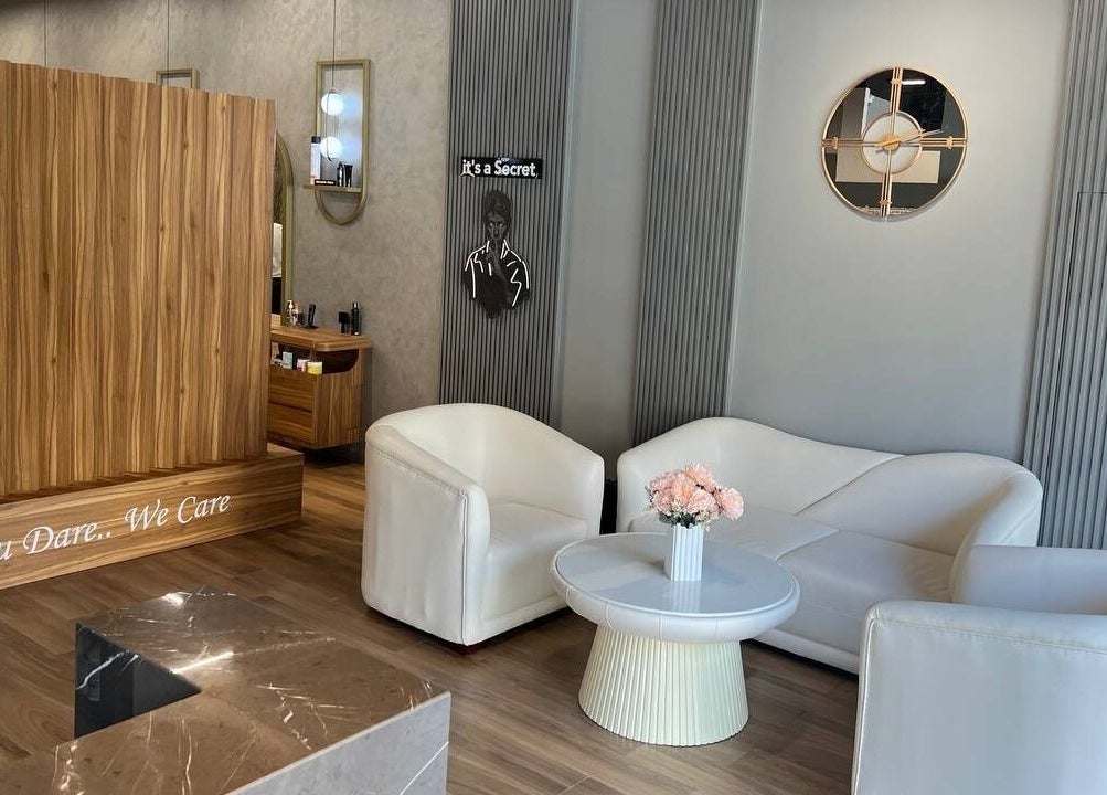 Reception area at Secret Care Barber Shop, Sharjah, features stylish white sofas and modern decor.