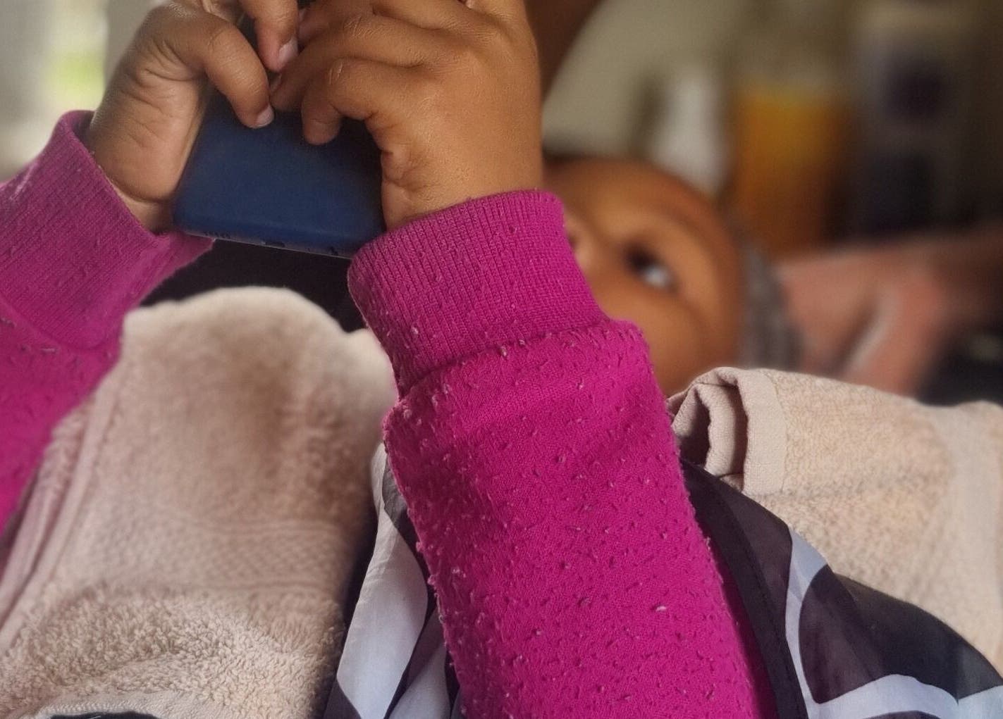 Child relaxing at Enhle Afro Salon in Mthatha, Eastern Cape, ZA, wrapped in towels, holding a phone.