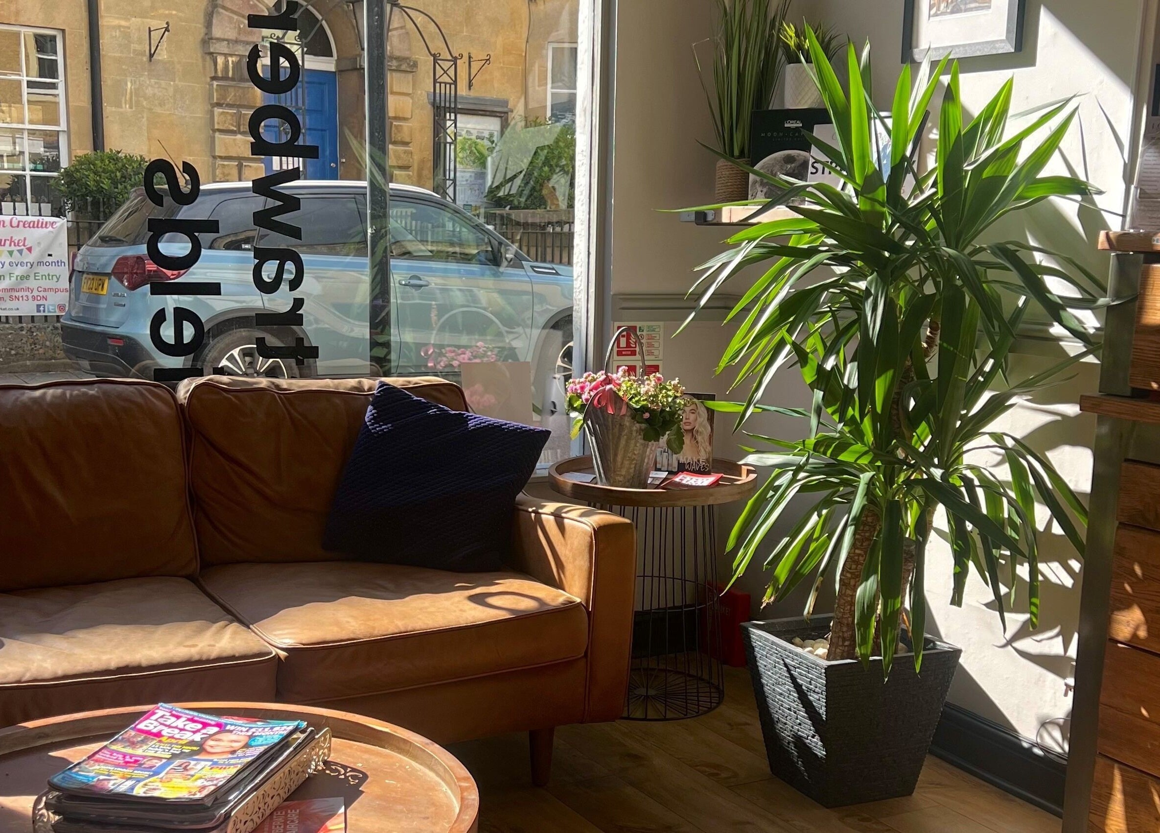 Relaxing seating area at Strawberry Fields Hair Design, Corsham, England, GB with leather sofa and plants.