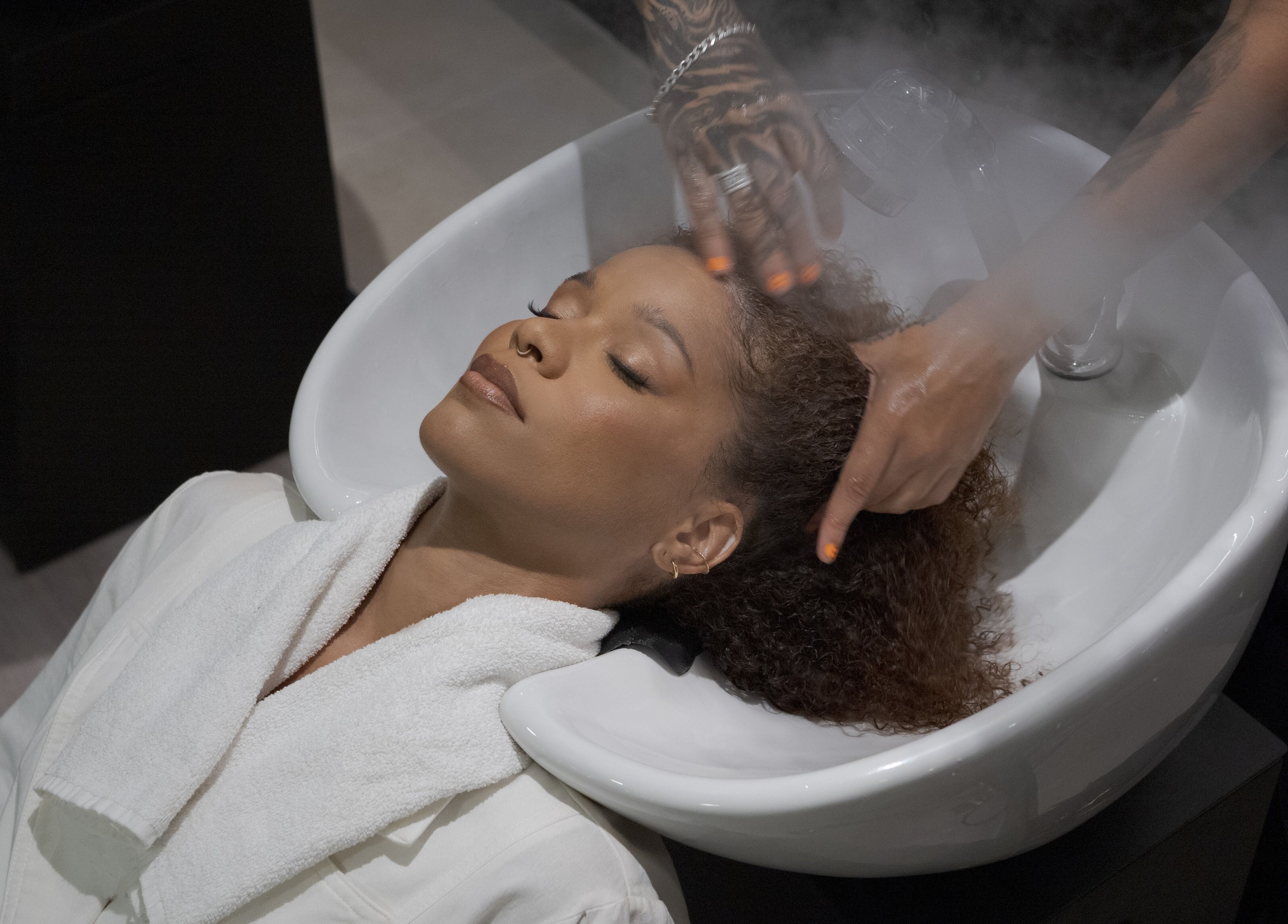 Cliente relaxa com lavagem de cabelo em Carol Scavello Barbearia, Bahia, Bahia, BR.